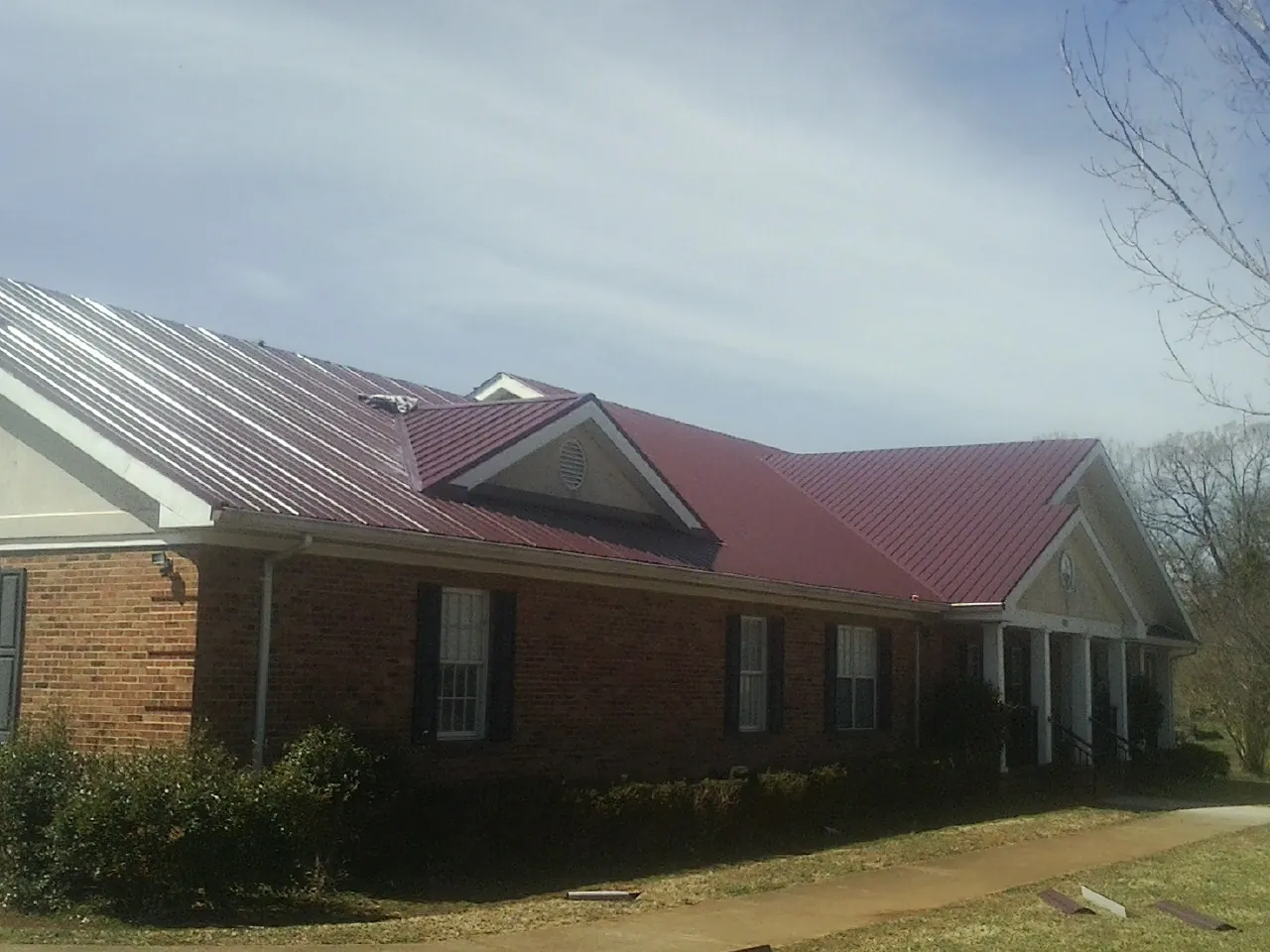Red metal roof with gabled entries on a long brick building, from a Hail Damage Roof Repair job in Jupiter
