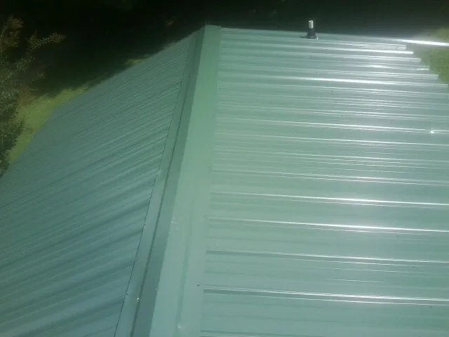 New green metal panels meeting at the ridge of a roof — Flat Roof Repair work by our crew in Jupiter