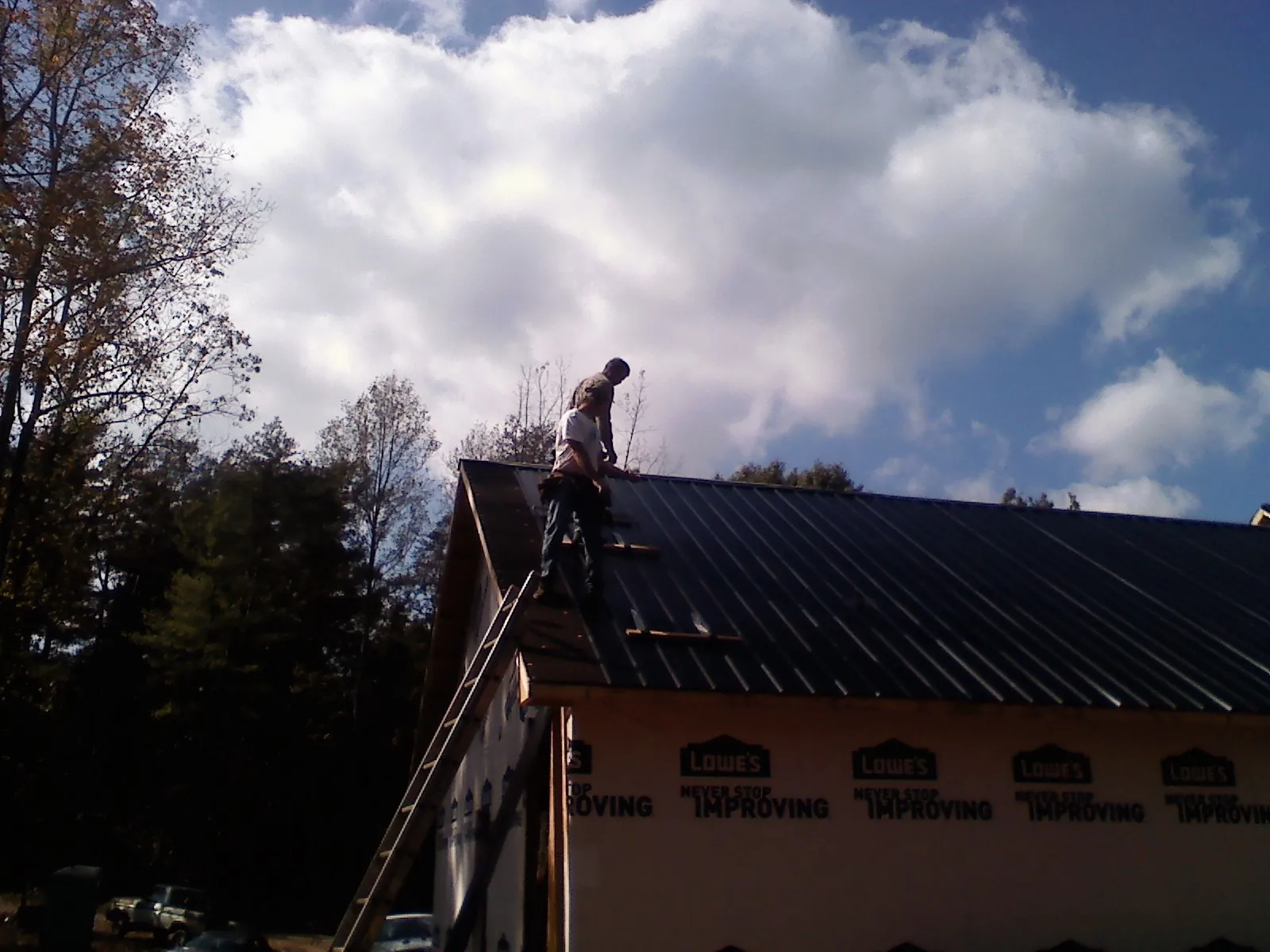 Roofer fastening dark metal panels high against a cloudy sky, from a Roof Inspection job in Jupiter